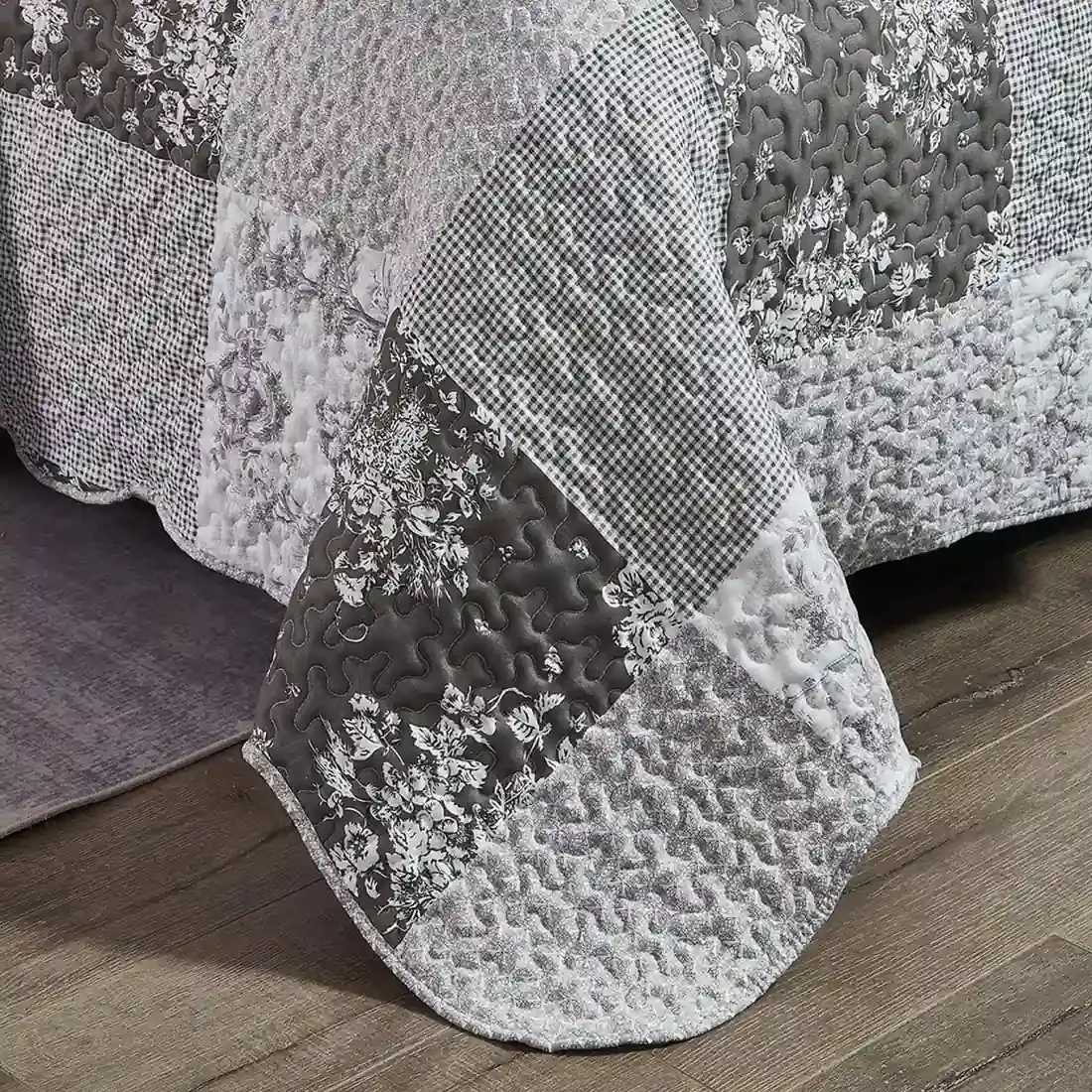 Detail of a grey quilt showcasing floral toile pattern, vermicelli stitching and scalloped edging.