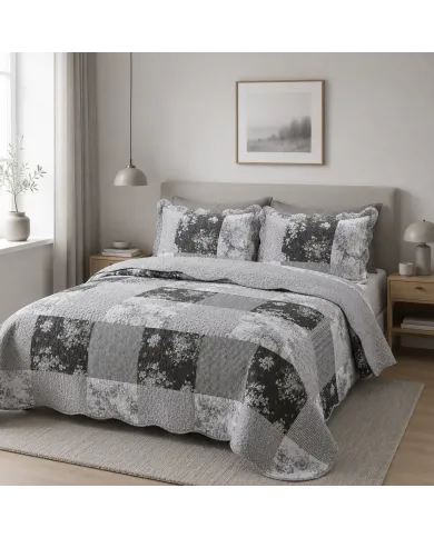 Grey quilt in a patchwork of floral and diamond motifs with matching pillowcases on a neatly made bed.