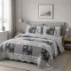 Grijze bedsprei in een patchwork van bloemen- en ruitmotieven met bijpassende kussenslopen op een netjes opgemaakt bed.