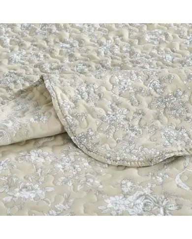 Close-up of a beige quilt, showcasing a floral toile pattern with a delicate stitching texture.