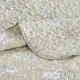 Close-up of a beige quilt, showcasing a floral toile pattern with a delicate stitching texture.