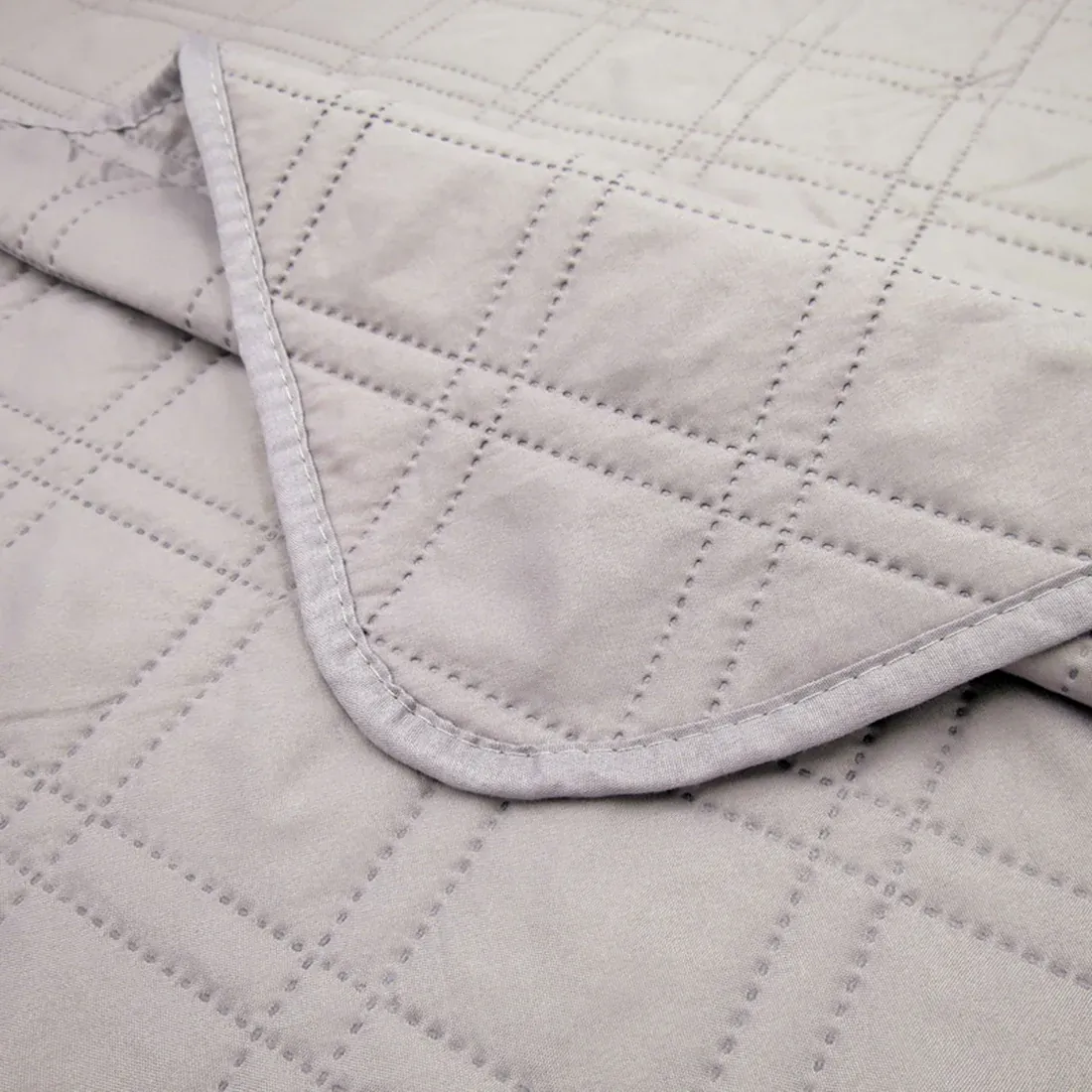 Close-up van een bedsprei grijs met een delicaat stikselpatroon.