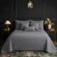 Een netjes opgemaakt bed met een bedsprei grijs in een kamer met twee nachtkastjes.