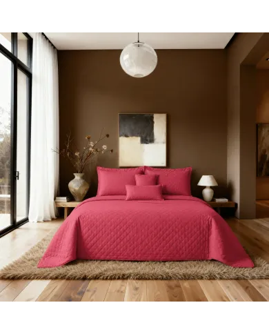 Een netjes opgemaakt bed met een bedsprei rood in een kamer met witte gordijnen en een nachtkastje.
