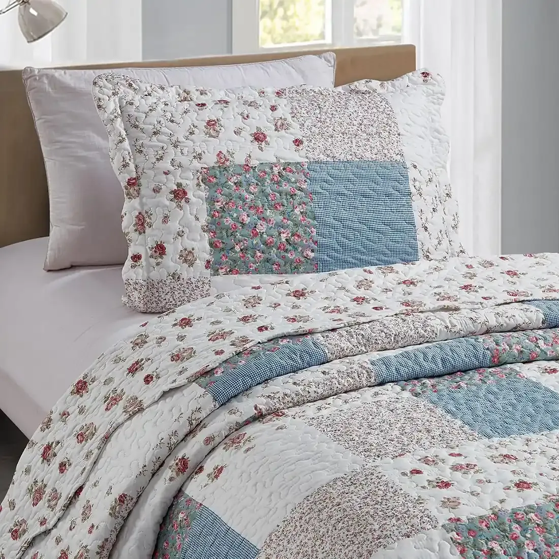 A blue pillowcase with matching bedspread on a cozy bed by a window.