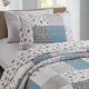 A blue pillowcase with matching bedspread on a cozy bed by a window.