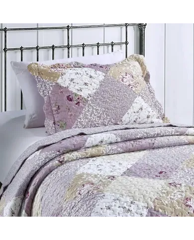 A floral pillowcase with matching bedspread on a cosy metal bed.