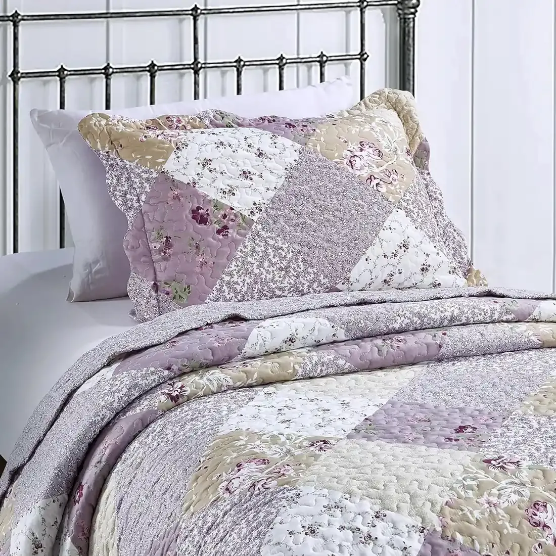 A floral pillowcase with matching bedspread on a cosy metal bed.