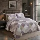 Een gezellige slaapkamer met een lavendelkleurig patchwork bloemen sprei en bijpassende kussensloop bloemen.