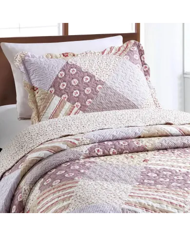 Een kussensloop roze die gebloemde, gestreepte en geruite vlakken combineert met bijpassende sprei op een knus bed.