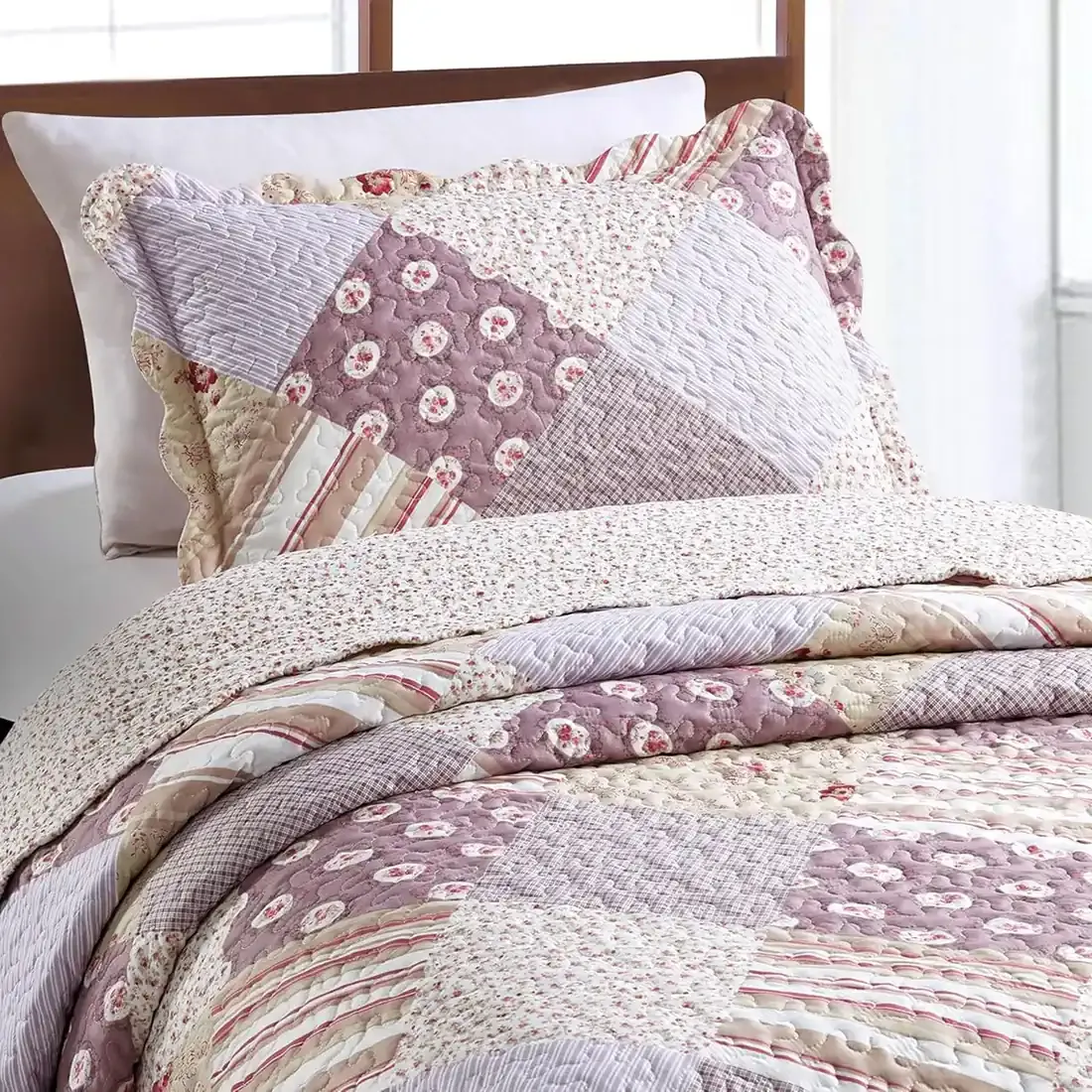Een kussensloop roze die gebloemde, gestreepte en geruite vlakken combineert met bijpassende sprei op een knus bed.