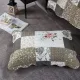 Een kussensloop beige met patchwork en Vintage Rose motieven rust op een grijze vloer met structuur.