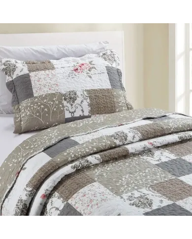A beige patchwork pillowcase with matching bedspread on a cosy bed by a window.