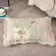Een kussensloop groen en roze met patchwork en bloemmotieven rust op een vloer met structuur.