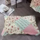A pink patchwork pillow in spring floral patterns rests on a textured grey floor.