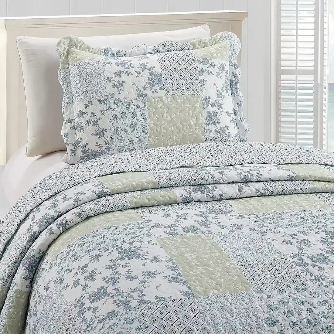 Een kussensloop wit en blauw met bijpassende sprei op een knus bed bij het raam.