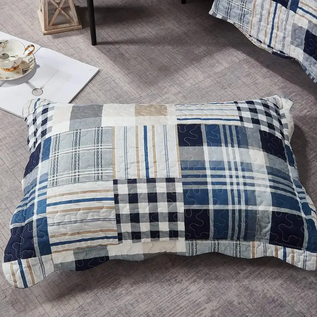 Een blauwe kussensloop met patchwork print rust op een grijze vloer met structuur.