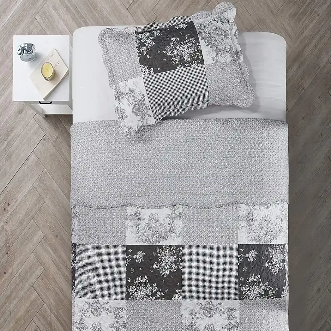 Bovenaanzicht van een grijze kussensloop op een bed, aangevuld met een bijpassende patchwork sprei.