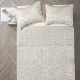 Top view of a beige pillowcase on a bed, complemented by a matching Toile quilt.