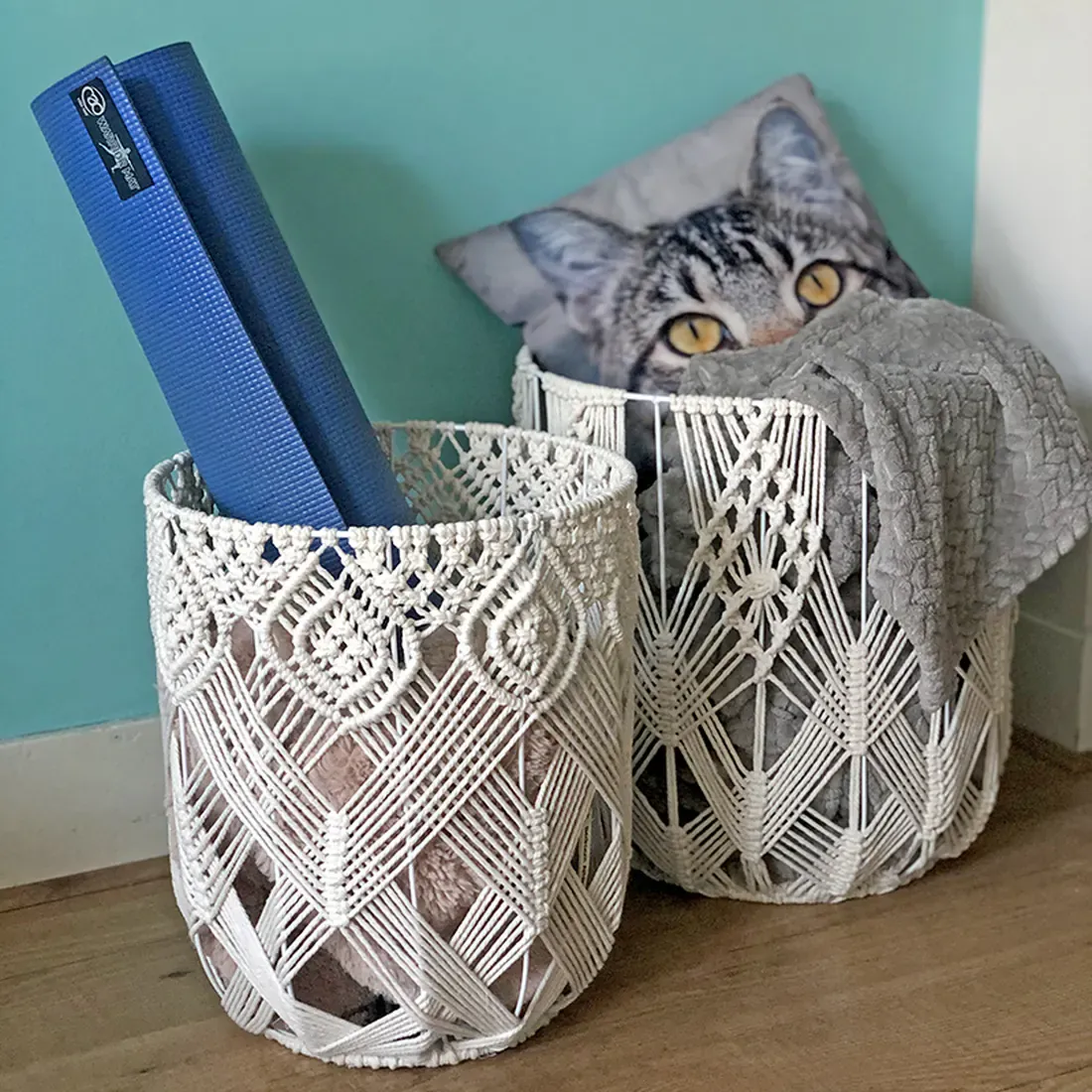 Two decorative macramé wire baskets hold a blue yoga mat, a cosy grey blanket and a cat-print cushion.