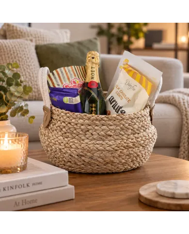 Een cadeau mand zeegras bevat een mini Moët champagneflesje, chocolaatjes en lekkernijen.
