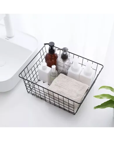 Black wire basket filled with various toiletries, a towel, and a plant in the background.