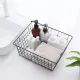 Draadmand zwart voor opberging gevuld met verschillende toiletartikelen, een handdoekje en een plant op de achtergrond.