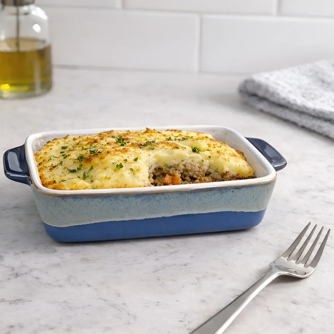 Shepherd's pie geserveerd in een eenpersoons ovenschaaltje met reactieve glazuurlaag, omringd door olijfolie.