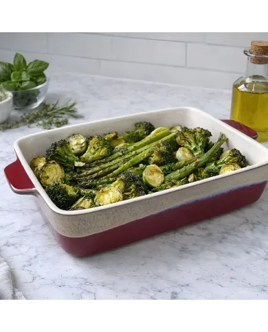 Roasted vegetables served in a reactive glaze oven dish, surrounded by fresh herbs, and olive oil.