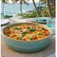 Een ronde ovenschaal met een pastagerecht, tegen de achtergrond van het uitzicht op de Caribisch zee.