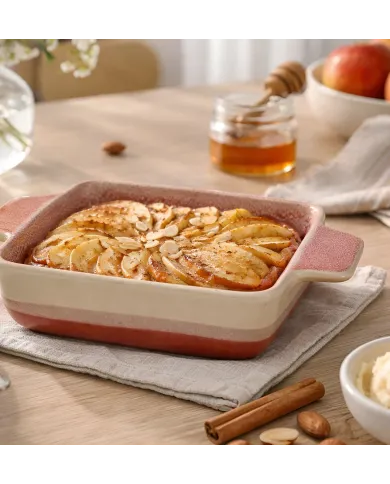 A square oven dish filled with an apple pie, alongside honey and a bowl of apples.