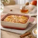 A square oven dish filled with an apple pie, alongside honey and a bowl of apples.