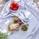 A dessert bowl with olives alongside a bowl of red tomatoes and a sandwich, with a striped cloth in the background.