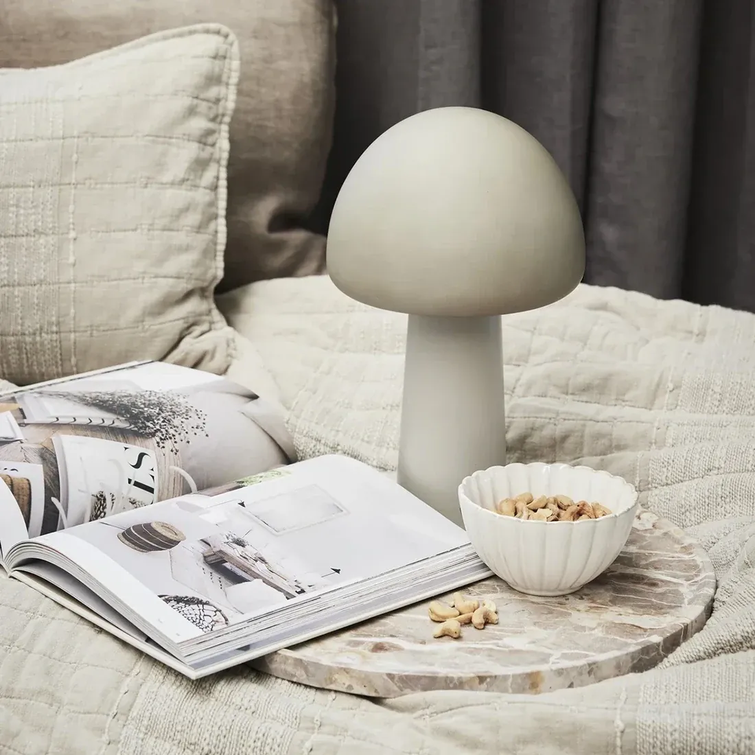 A dessert bowl with nuts sits on a marble tray beside a mushroom lamp.