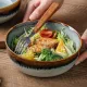 Een close-up van een bohemien soepkom gevuld met salade, kip en broccoli, met een vork ernaast.