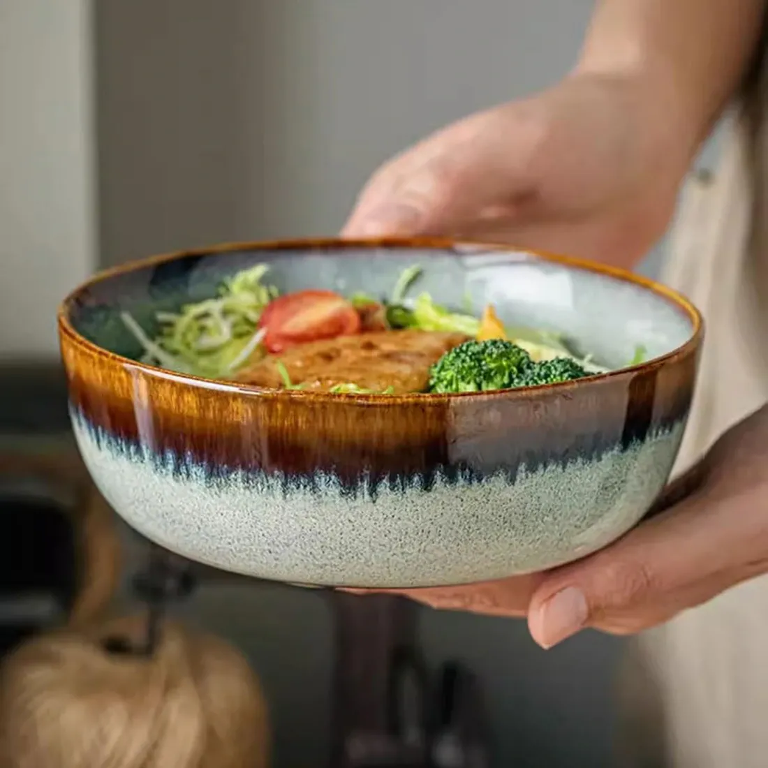 Een close-up van een bohemien soepkom gevuld met salade, kip en broccoli, vastgehouden door twee handen.