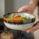 Een close-up van een bohemien soepkom gevuld met salade, kip en broccoli, vastgehouden door twee handen.