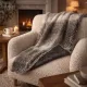 Cosy armchair with a soft grey faux fur throw blanket in a warm living room with a lit fireplace.