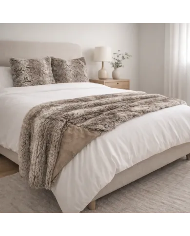 Knusse slaapkamer met een taupekleurige plaid op het bed en bijpassende exemplaren van het imitatie bont kussen.