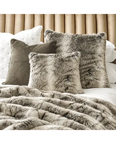 Een zacht bed met een plaid van imitatiebont en een variatie van het grijze kussen van imitatiebont.
