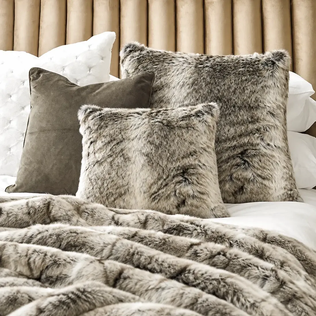 Plush bed with a faux fur throw and a variety of faux fur grey cushions.