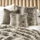 Plush bed with a faux fur throw and a variety of faux fur grey cushions.