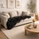 Cosy neutral living room with a cream sofa and a black sheepskin rug draped over it.