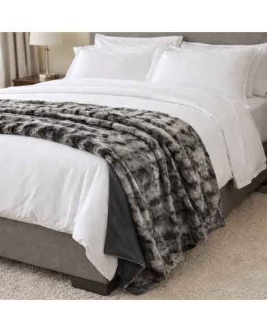 Cosy made bed with white sheets, pillows, and a silver grey faux fur throw blanket in a modern bedroom.