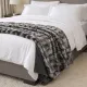 Een gezellig opgemaakt bed met witte lakens, kussens en een zilvergrijze plaid van imitatie bont in een moderne slaapkamer.