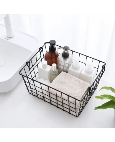Black wire basket filled with various toiletries, a towel, and a plant in the background.
