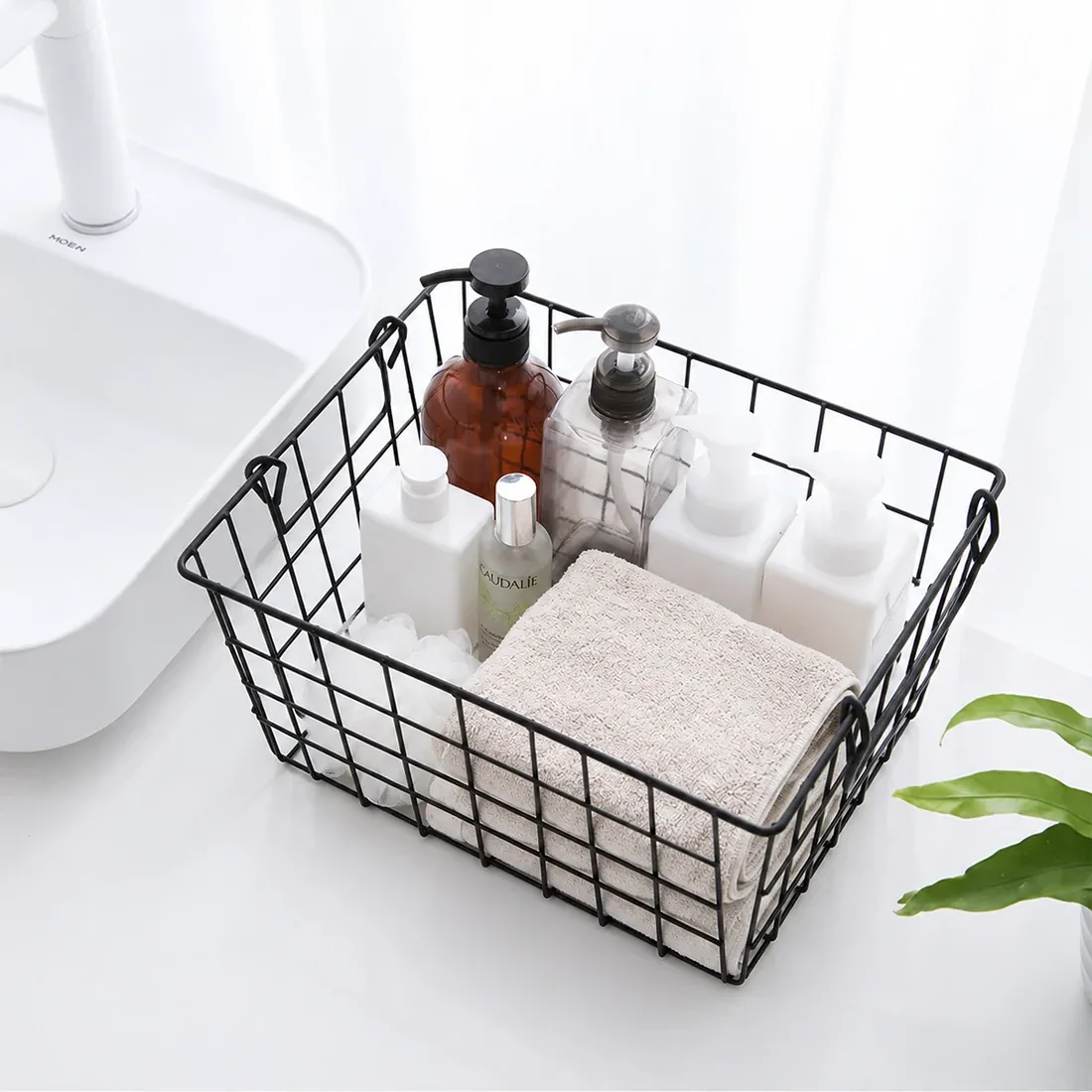 Draadmand zwart voor opberging gevuld met verschillende toiletartikelen, een handdoekje en een plant op de achtergrond.