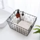 Draadmand zwart voor opberging gevuld met verschillende toiletartikelen, een handdoekje en een plant op de achtergrond.