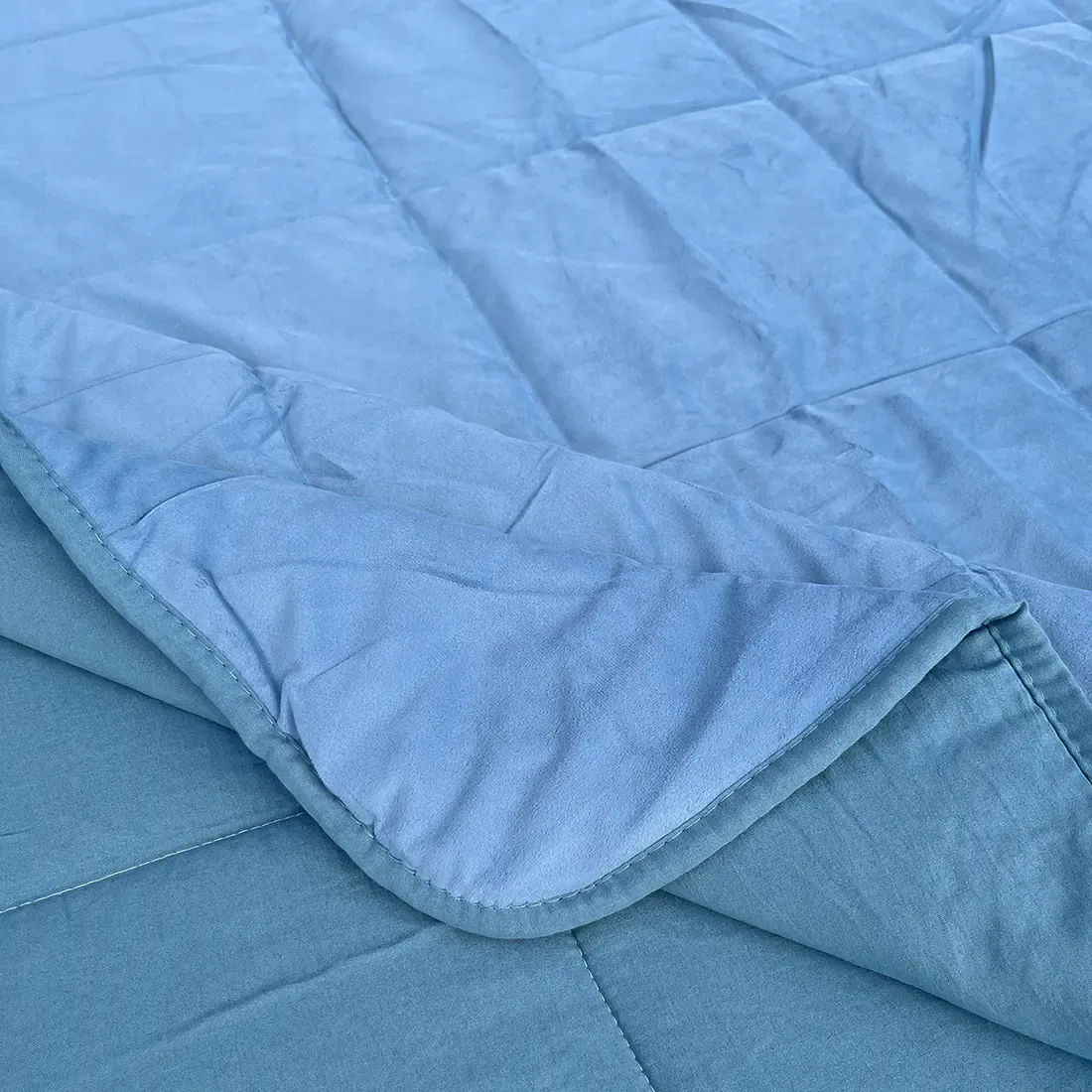 Close-up van een fluwelen dekbed zonder overtrek blauw met vierkante stiksels en een contrasterende onderkant.