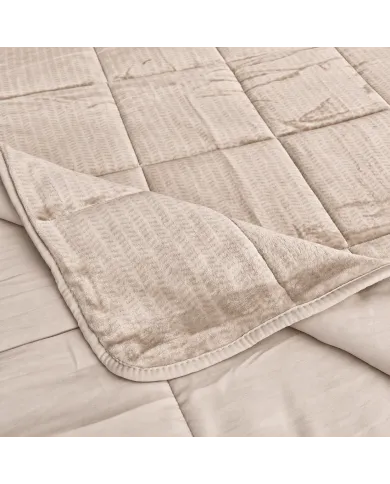 Close-up of a velvet bedspread with textured square stitching and contrasting underside.